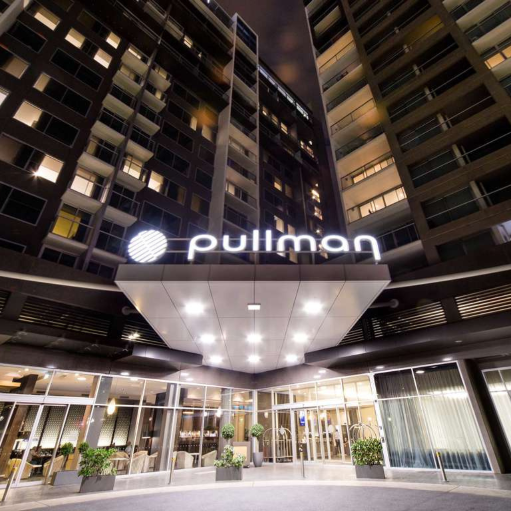 Night view of the Pullman hotel entrance with a glowing sign and illuminated canopy over glass doors