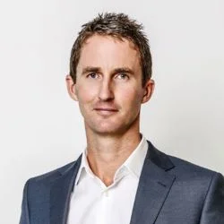 Professional headshot of a man in a navy suit and white shirt against a light background.